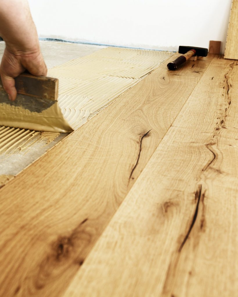 Man applying glue for laying finished parquet flooring, close-up